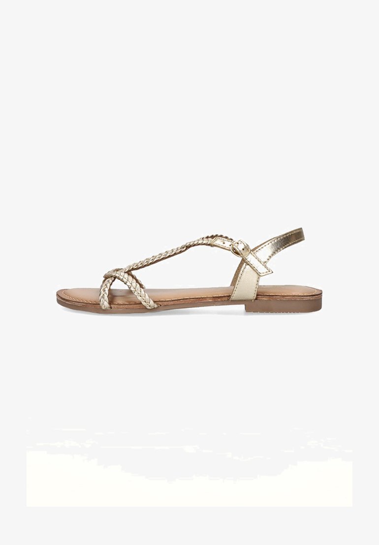 Sandal de oro trenzado con suela plana, que cuenta con una delgada correa para el tobillo y un diseño de punta abierta, exhibida sobre un fondo blanco.