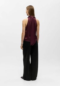 Bordeauxfärgad satinblus med en halsknut, matchad med vida svarta byxor. Slät textur med en elegant design. Bakifrån som visar detaljer.