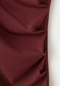 Tissu bordeaux avec plis horizontaux visibles et texture tricotée fine, présenté sur un fond blanc.