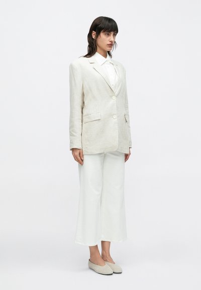 Hellbeiger Leinenblazer mit einem einzelnen Knopf, kombiniert mit weißen Hosen mit weitem Bein und hellen Slippern. Glatte Textur und minimalistisches Design.