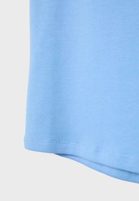 Svijetloplavi pamučni materijal s vidljivim šavovima duž ruba na jednostavnoj svijetloj pozadini.