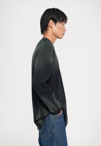 Svart langermet skjorte med gradient-effekt, myk tekstur, avslappet passform og ribbet halslinning, kombinert med lyseblå jeans.