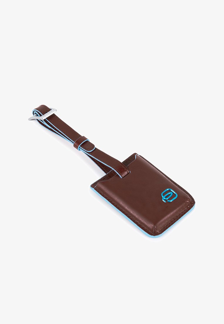 Tag per bagaglio in pelle marrone con cuciture blu e una fibbia metallica. Presenta uno slot per l'identificazione e ha una forma rettangolare arrotondata.