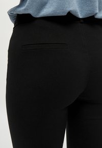 Zwarte broek van een gestructureerde stof met een enkele achterzak, een slim fit ontwerp en subtiele stikdetails.