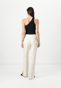 Top nero monospalla abbinato a pantaloni palazzo crema con spacchi laterali e tasca sul retro, mostrato su uno sfondo bianco uniforme.