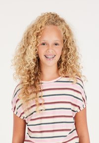 Dívka s kudrnatými blond vlasy, která má na sobě krátký rukáv, pruhované tričko v růžové a krémové barvě s tmavě modrými akcenty a kulatým výstřihem.
