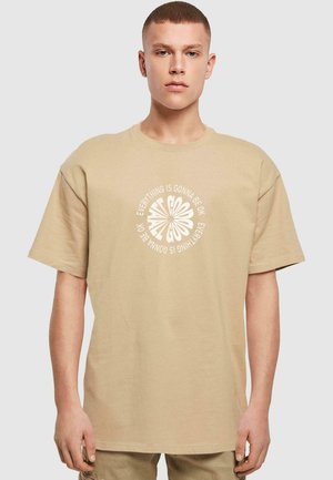 Beige bomulds t-shirt med løs pasform, korte ærmer og et cirkulært hvidt grafisk tekstdesign med teksten "Alt sammen bliver godt."