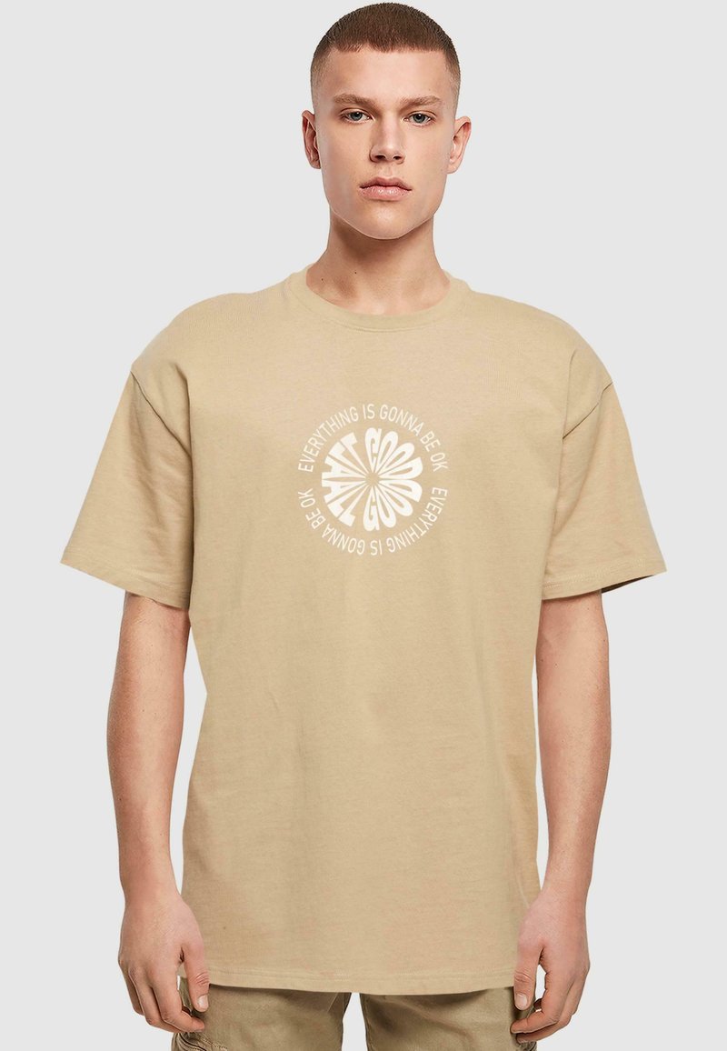 Beige bomulds t-shirt med løs pasform, korte ærmer og et cirkulært hvidt grafisk tekstdesign med teksten "Alt sammen bliver godt."