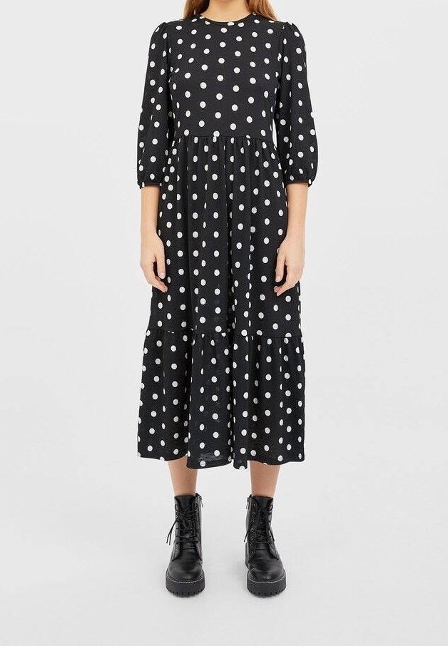 Zwarte midi-jurk met witte polka dots, ronde halslijn, driekwart mouwen, geplooide zoom, gecombineerd met zwarte enkellaarzen.