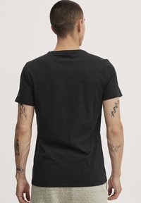 Czarny t-shirt z krótkim rękawem o dopasowanym kroju. Prosty okrągły dekolt i gładki materiał. Widoczne charakterystyczne tatuaże na ramionach.