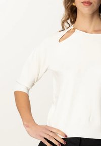 Maglione bianco con scollo rotondo e dettaglio a occhiello sulla spalla. Maniche a tre quarti, orlo a costine e texture morbida.