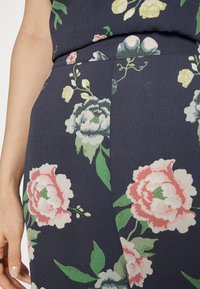 Um tecido com padrão floral em azul marinho apresenta folhas verdes e flores rosa, brancas e azuis. O material tem uma aparência texturizada.