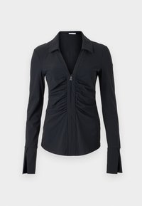 Maglietta nera a maniche lunghe con scollo a V profondo e design arricciato sul davanti. Presenta una chiusura con zip e polsini a spacco. Realizzata in tessuto morbido.