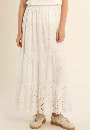 Gonna bianca alla caviglia con motivi traforati ricamati, vita elasticizzata, indossata con sneakers beige con lacci su sfondo neutro.