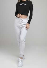 Svart långärmad croppad topp med vit text, i kombination med ljusgrå sweatpants med elastiska muddklackar och dragsko i midjan. Vita sneakers.