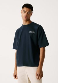 Navyblaues Baumwoll-T-Shirt mit kurzen Ärmeln, rundem Ausschnitt und einem weißen Red Bull Racing-Logo auf der linken Brust. Weicher und geschmeidiger Stoff.