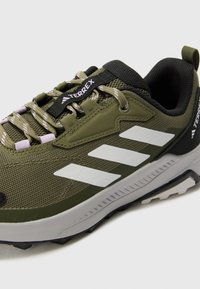 Men's green athletic shoes with mesh upper, black accents, and white stripes. Features rugged sole and reflective laces for traction.