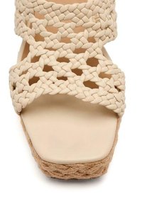 Sandales à plateforme tissées beiges avec des brides croisées en tresse et une semelle en fibre naturelle, présentant un design à bout carré.