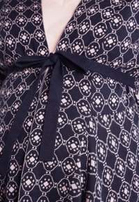 Marinblå stickad klänning med ett geometriskt mönster i ljusrosa, med en omslagdesign och en knytning i midjan. Mjuk textur, långa ärmar.