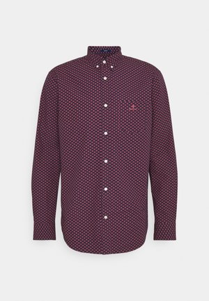 Chemise homme à manches longues avec une base bleu marine et un petit motif floral rouge, comprenant une poche avant et des boutons blancs.