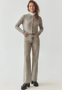 Grau gestrickte Strickjacke mit Kragen und weißen Knöpfen, kombiniert mit hochtaillierten grauen Schlagjeans und schwarzen Plateauschuhen.