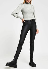 Grå rullkrage med ribbat mönster och puffärmar, i kombination med högmidjade svarta jeans i läderlook och kraftiga svarta ankelstövlar.