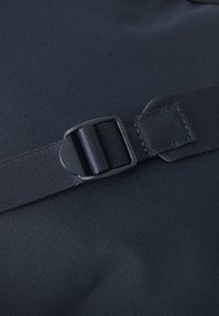 Marinfärgad tygpouch med en texturerad yta, säkrad med ett svart justerbart band och en plastspänne för stängning.
