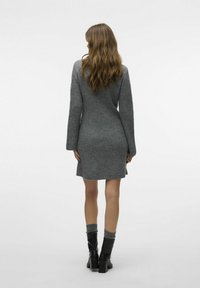 Robe en tricot gris à côtes avec des manches longues et une coupe ajustée, se terminant au-dessus du genou. Associée à des bottes noires jusqu'au genou et des chaussettes grises.