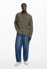 Tume roheline pikkade varrukatega särk, millel on mitmevärviline muster; sobitatud laia sinise teksapükse ja heledate tossudega. Nuppudega mudel kraega.