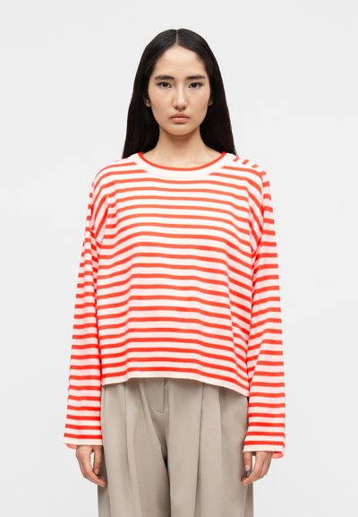 Pull crop à manches longues rayé blanc et corail, doté d'un col rond et d'un tissu texturé. Associé à un pantalon léger plissé.