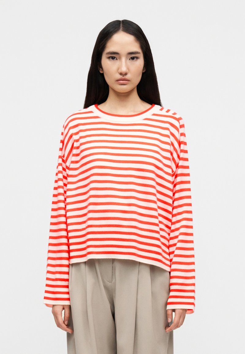 Pull crop à manches longues rayé blanc et corail, doté d'un col rond et d'un tissu texturé. Associé à un pantalon léger plissé.