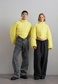 Yellow puffer jackets with oversized sleeves, paired with gray and black loose-fitting pants. Jackets feature a zip closure and textured surface.