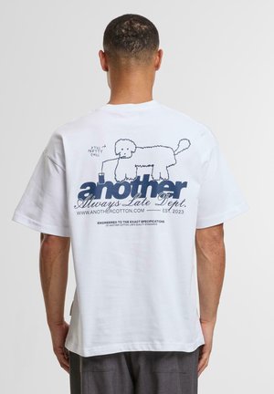 White cotton t-shirt featuring a navy graphic of a dog with a drink. Text includes "another" and "Always Late Dept." in bold font.