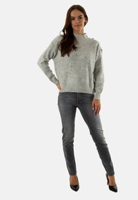 Maglione grigio lavorato a maglia con motivo testurizzato, collo rotondo e dettagli sulle spalle, abbinato a jeans grigi slim-fit e scarpe con tacco nere.