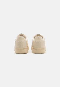Sneakers in pelle beige con una texture liscia, punta rotonda e colletto imbottito, caratterizzati da una suola spessa color crema.