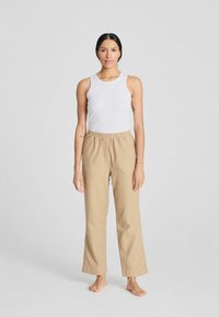 Top blanco sin mangas y pantalones beige, ligeros, con cintura elástica. Los pantalones tienen un corte holgado, piernas rectas y una textura sutil.