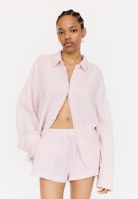 Lichtroze katoenen loungewearset met een knoopsluiting shirt met een zachte textuur en bijpassende korte broek met tunnelkoord. Het shirt heeft een losse pasvorm.