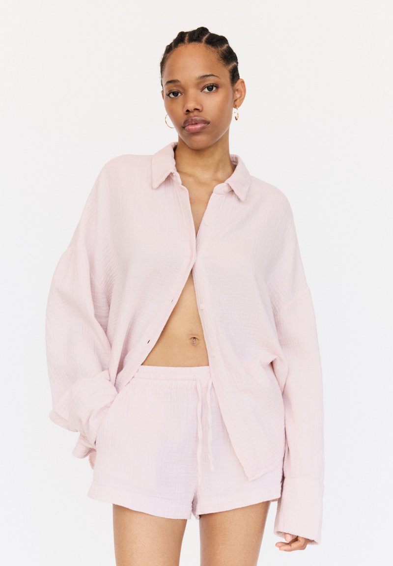Lichtroze katoenen loungewearset met een knoopsluiting shirt met een zachte textuur en bijpassende korte broek met tunnelkoord. Het shirt heeft een losse pasvorm.