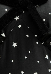 Tissu noir avec des motifs d'étoiles blanches, avec un accent en velours doux au niveau du col. Détails froncés près de la poitrine pour une texture.