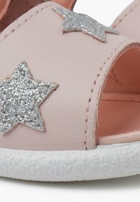 Růžová kožená sandál se třpytivými stříbrnými hvězdnými ozdobami, otevřený design špičky a texturovaná bílá gumová podrážka.