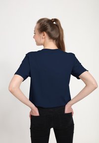 Navy blue short-sleeved t-shirt with a crew neck, made of smooth fabric. Worn with black jeans, showing a casual fit from the back.