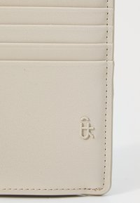 Cardholder din piele bej, cu multiple sloturi, suprafață texturată și logo embosat. Prezintă cusături vizibile și un design minimalist.
