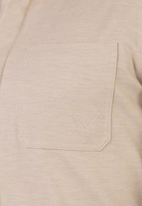 Poche de chemise en tissu beige avec un motif subtil de feuille brodé en fil assorti dans le coin inférieur droit.