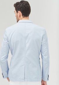 Světle modrý blazer s hladkou bavlněnou směsí, s jedním rozvorem na zadní straně a jemným švem. Černé knoflíky zdobí manžety.