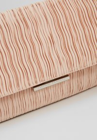 Pochette plissée rose pâle avec une fermeture argentée horizontale gravée "Loeffler Randall", posée sur une surface blanche.