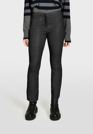 Zwarte synthetische broek met een elastische tailleband, slim fit en een gladde textuur. Gestyled met een geribbelde grijs- en marineblauwe gestreepte sweater en zwarte laarzen.