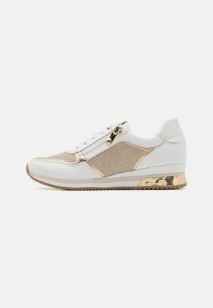 Sneaker bianco con lato testurizzato accentuato da dettagli dorati, particolari metallici e chiusura con zip. La suola è marrone chiaro con un design a motivi.