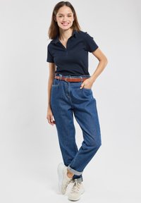 Polo navy, jeans blu a vita alta, cintura in pelle marrone, sneakers bianche. Vestibilità rilassata con risvolti sui jeans, tessuto dalla trama liscia.