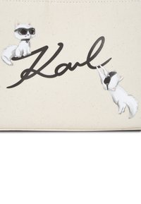 Borsetta in canvas con due gatti cartoon che indossano occhiali da sole, con la firma nera "Karl" e uno sfondo crema.