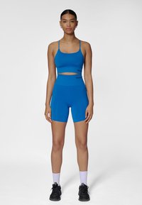 Blå sport-bh och höga midjeshorts i set, tillverkade av stretchigt tyg med slät textur och minimala sömmar. Har tunna band och logotypdetaljer.